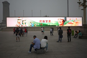 people in front of a large video display at Tiananmen Square