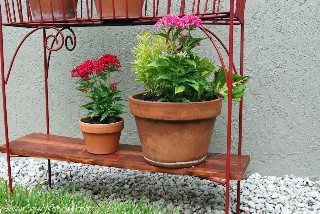 Bottom view of a red wire rack with a wood shelf and potted plants.