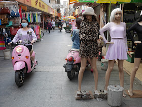 young woman wearing a face mask riding a pink motorbike past mannequins in Yangjiang, China