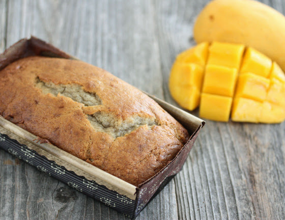 photo of a loaf of Mango Banana Bread with fresh mango in the background