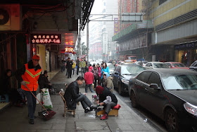 a shoe shining on a sidewalk in Hengyang and several people looking at me