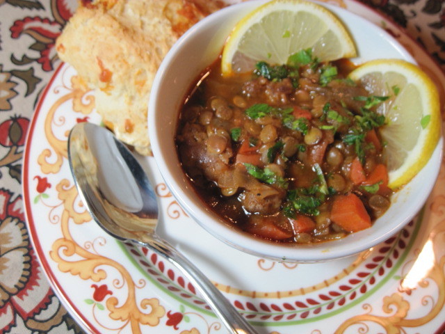 A bowl of Lentil Stew with a spoon and lemons.