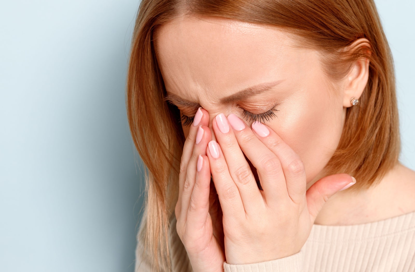 A woman holds her face due to sinus and head pressure and pain from allergies
