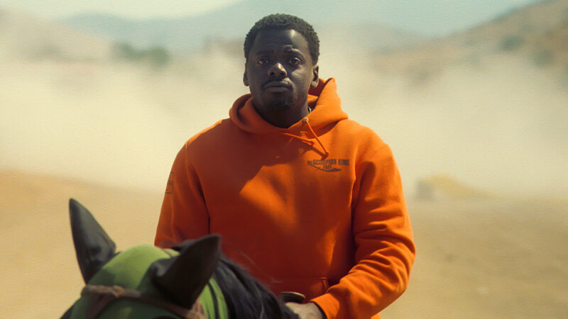 A man in a orange sweatshirt rides a horse in the desert