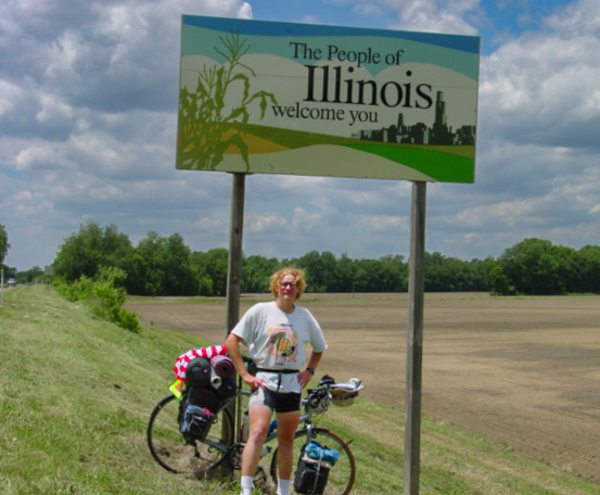 Bicyclist stands under a sign that reads: The people of Illinois welcome you. 
