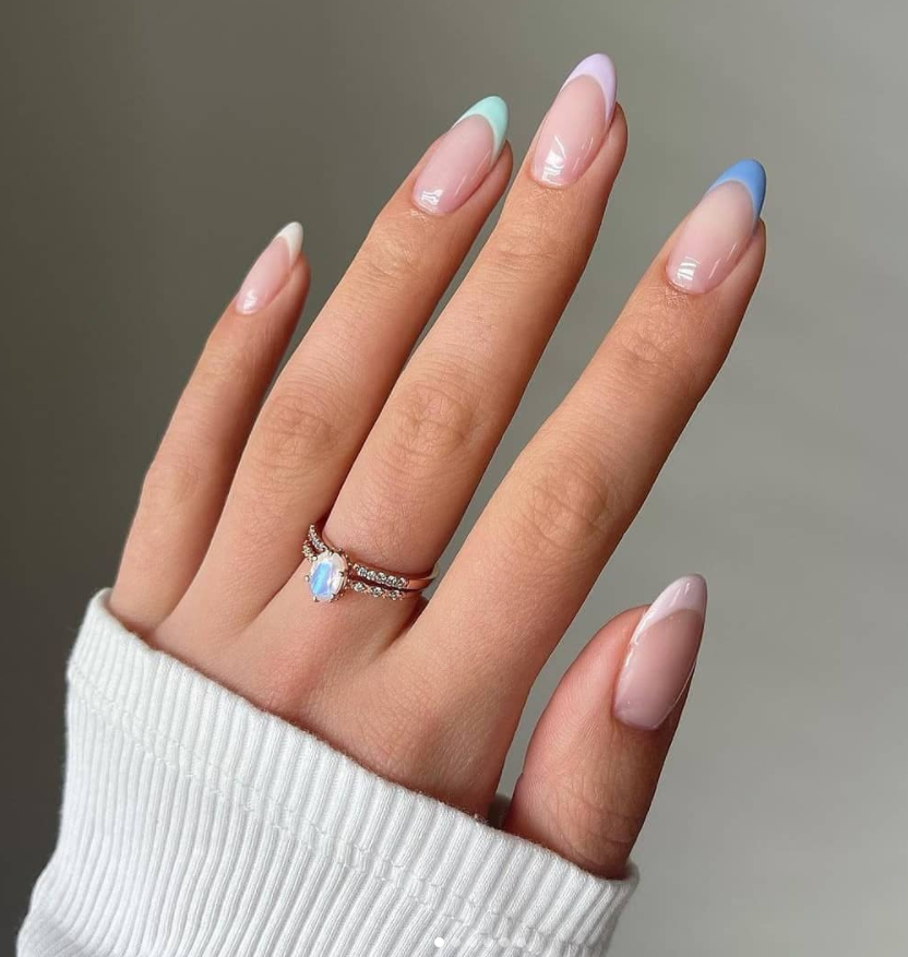 Mão de uma pessoa com unhas no formato almond e com francesinhas em tons pastéis, são eles: rosa, lilás, azul e off-white. 