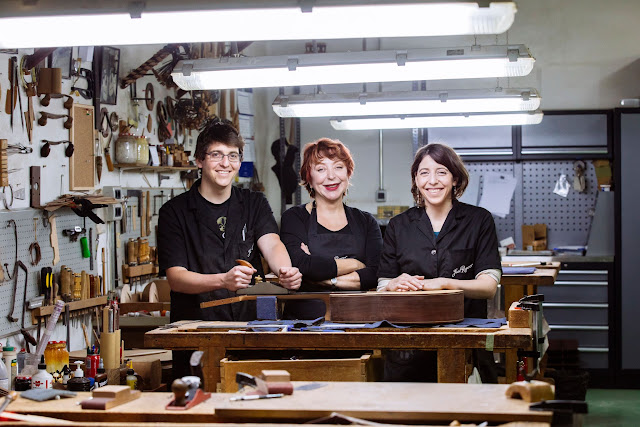 3 personas vestidas de negro en un taller rodeadas de herramientas.