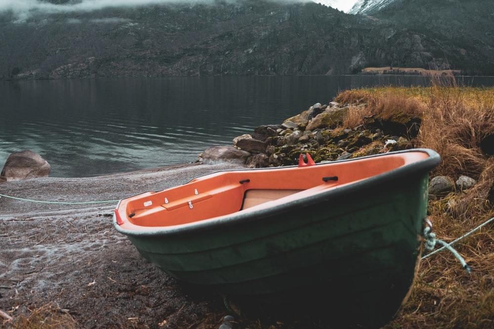 orange and white boat on brown soil near body of water during daytime