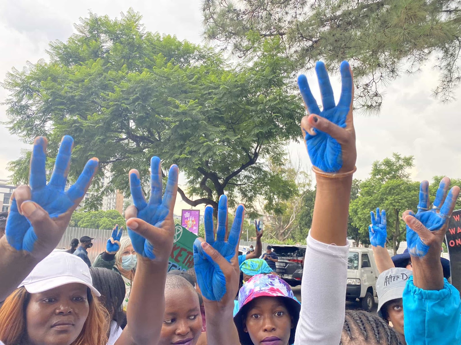 Women look to camera and hold up their hands for a three finger salute, their fingers daubed in bright blue paint