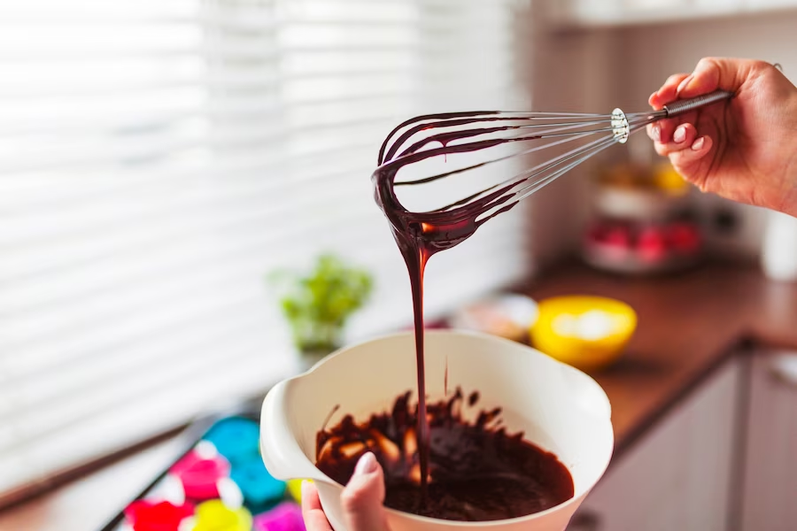 Whisked chocolate dripping from a hand-held whisk into a bowl