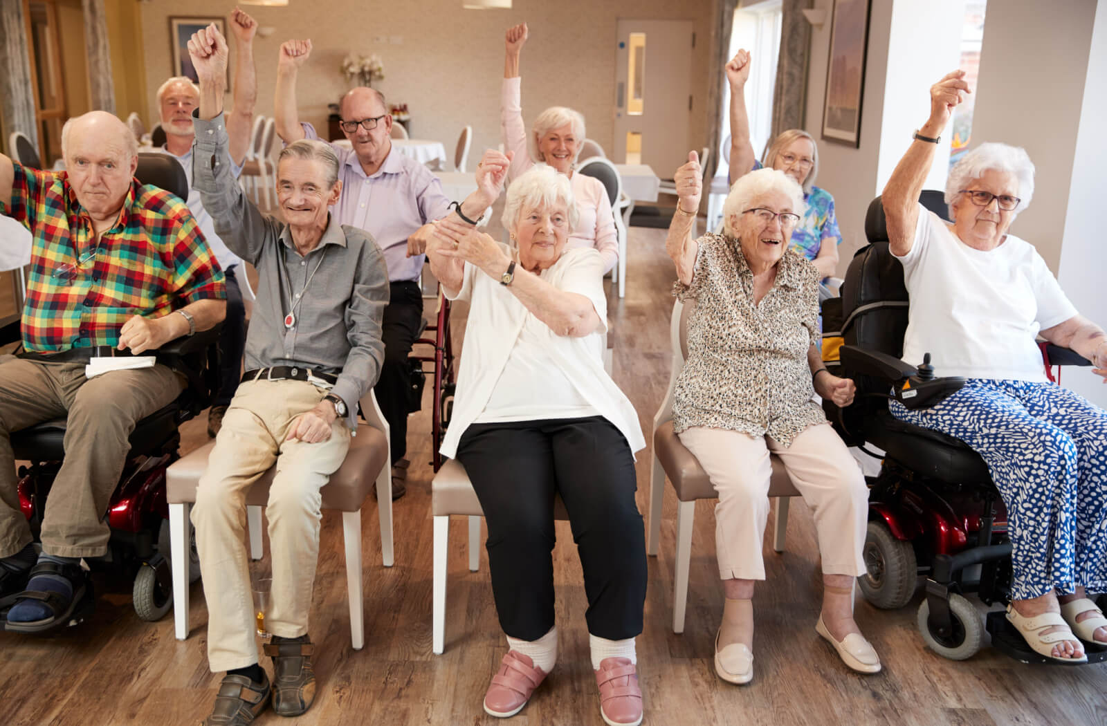 A group of seniors in an audience, each raising their right hand in a fist, some are smiling