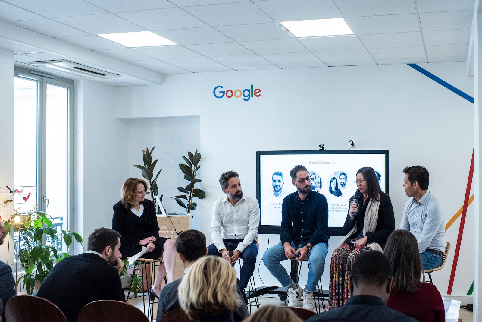 A group of five people are speaking to an audience in a room with the Google logo on the wall