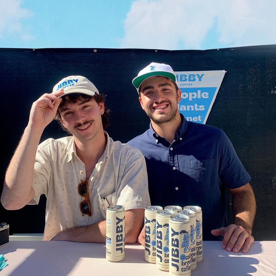 Jibby Coffee Smile ABC—An image of Jibby Coffee founders, James Reina and Alvaro Ortega sitting next to each other with several cans of their CBD Cold Brew Coffee on the table in front of them.