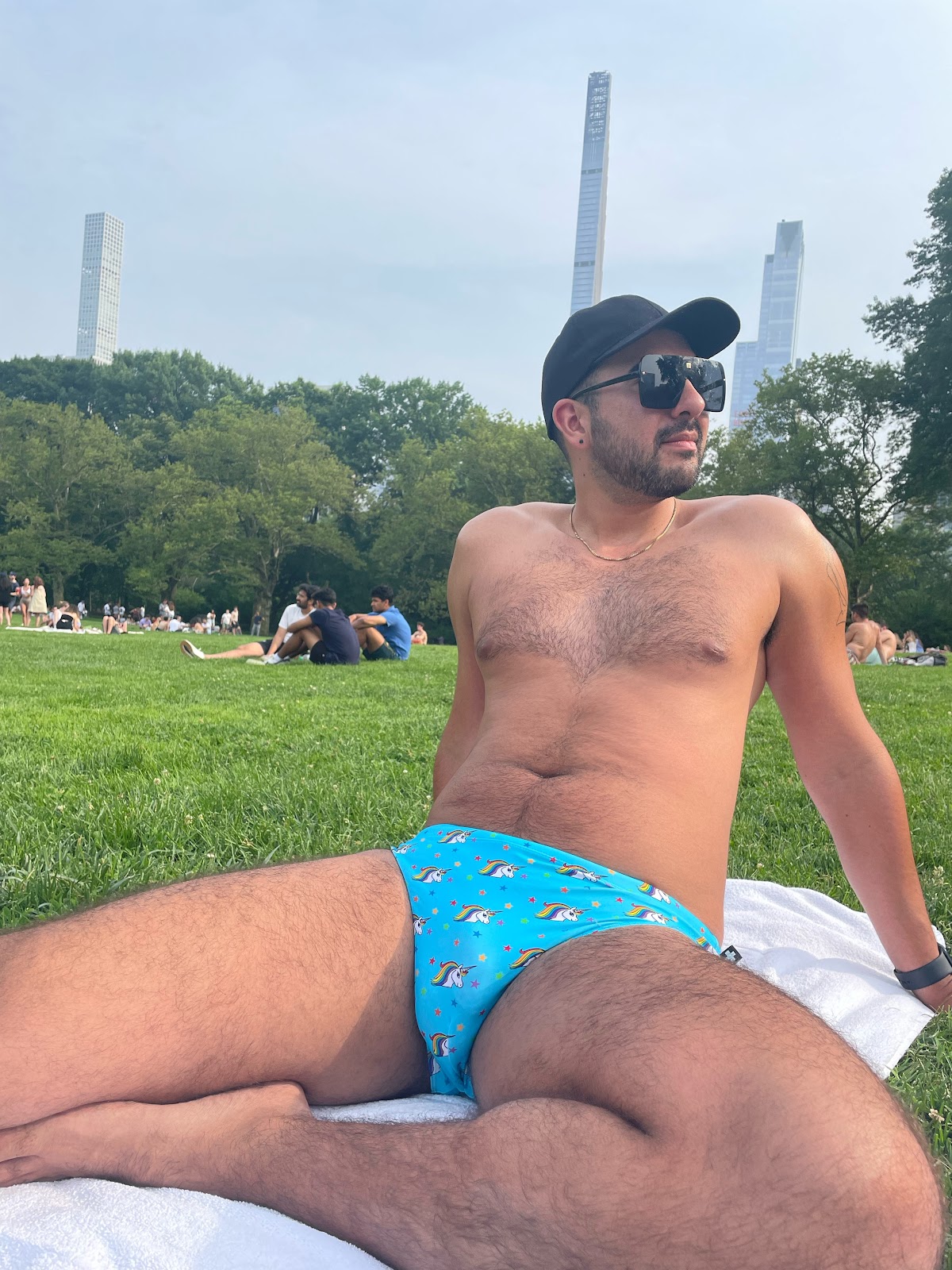 gay male wearing unicorn printed speedo in new york city summer central park on the grass lying on a towel