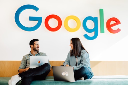 A man and woman sitting with laptops open using Google.