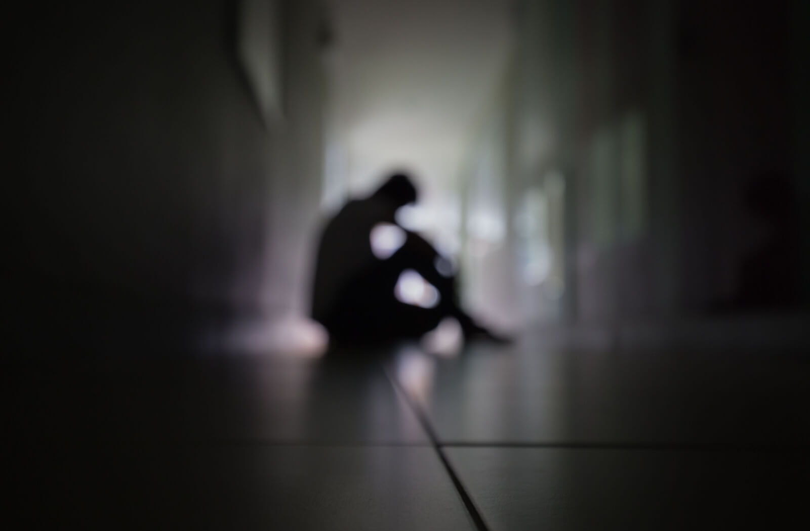 A silhouette of a man sitting in a corner of a dark room.