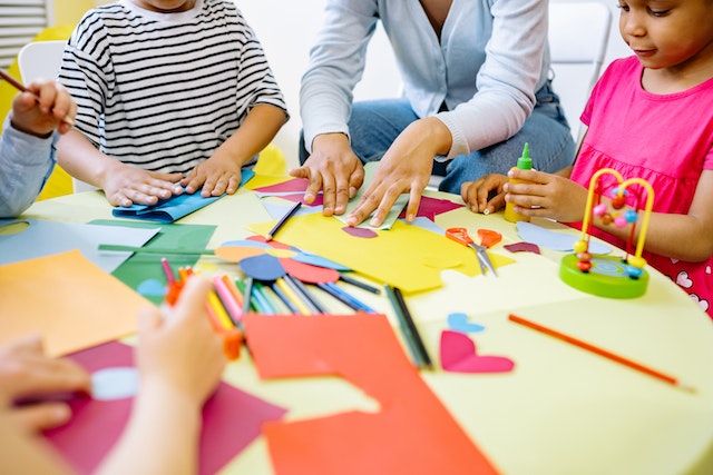 Teacher and children doing arts and crafts at a table 