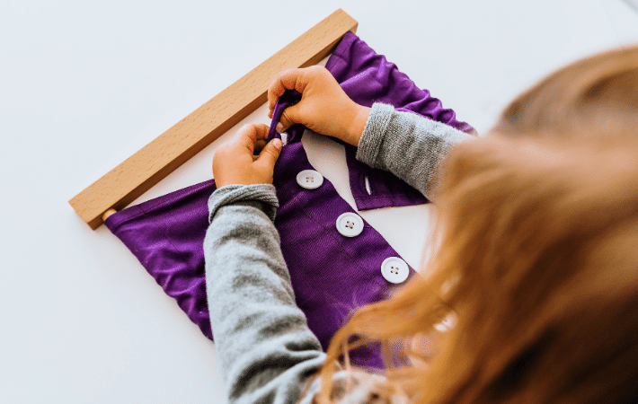 A little girl completing a Montessori activity in which she learns how to button up purple material independently.