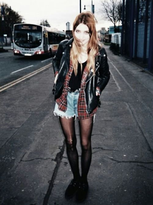 Woman waiting for a bus wearing a leather jacket, plaid and short shorts