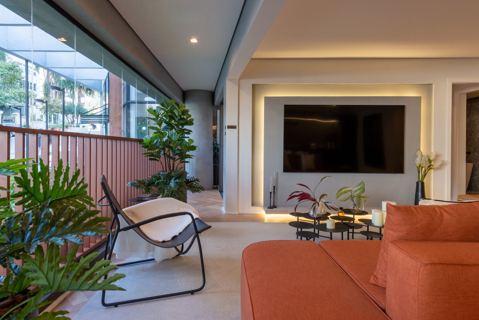 Apartamento com varanda integrada a sala de estar, com vasos de plantas e sofá alaranjado