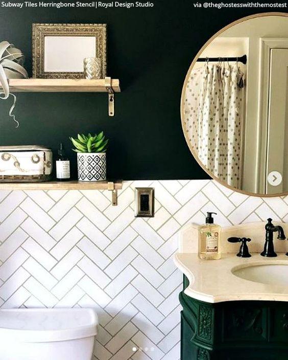 Banheiro com meia parede revestida de azulejo subway tiles branco em formato zig zag e outra metade pintada de verde, prateleiras de madeira, gabinete verde e pia em tom neutro com torneira preta.