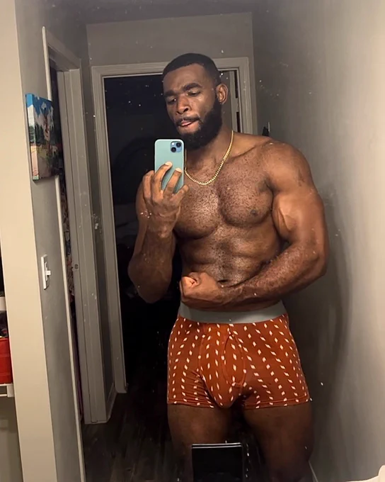 Marshall Price posing and flexing for the camera while taking an iPhone Mirror selfie in a red and white boxer briefs