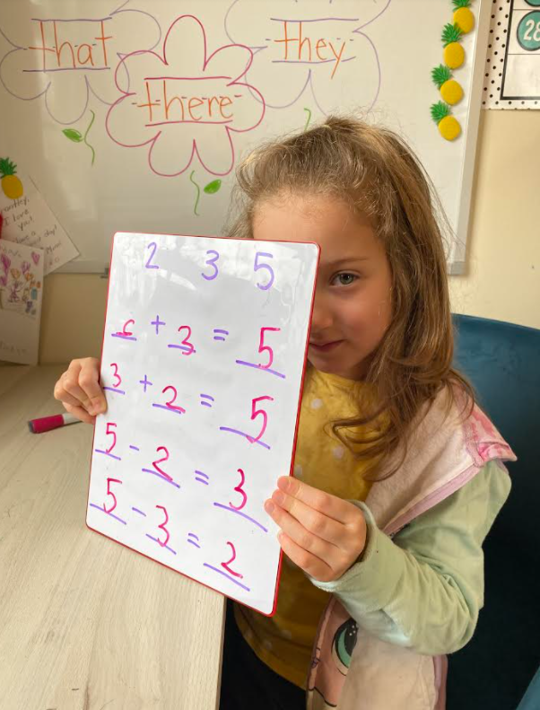 young blond girl holding up mathematics work
