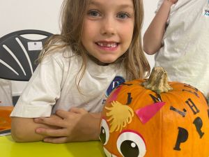 Child proudly showcasing their creatively decorated pumpkin.