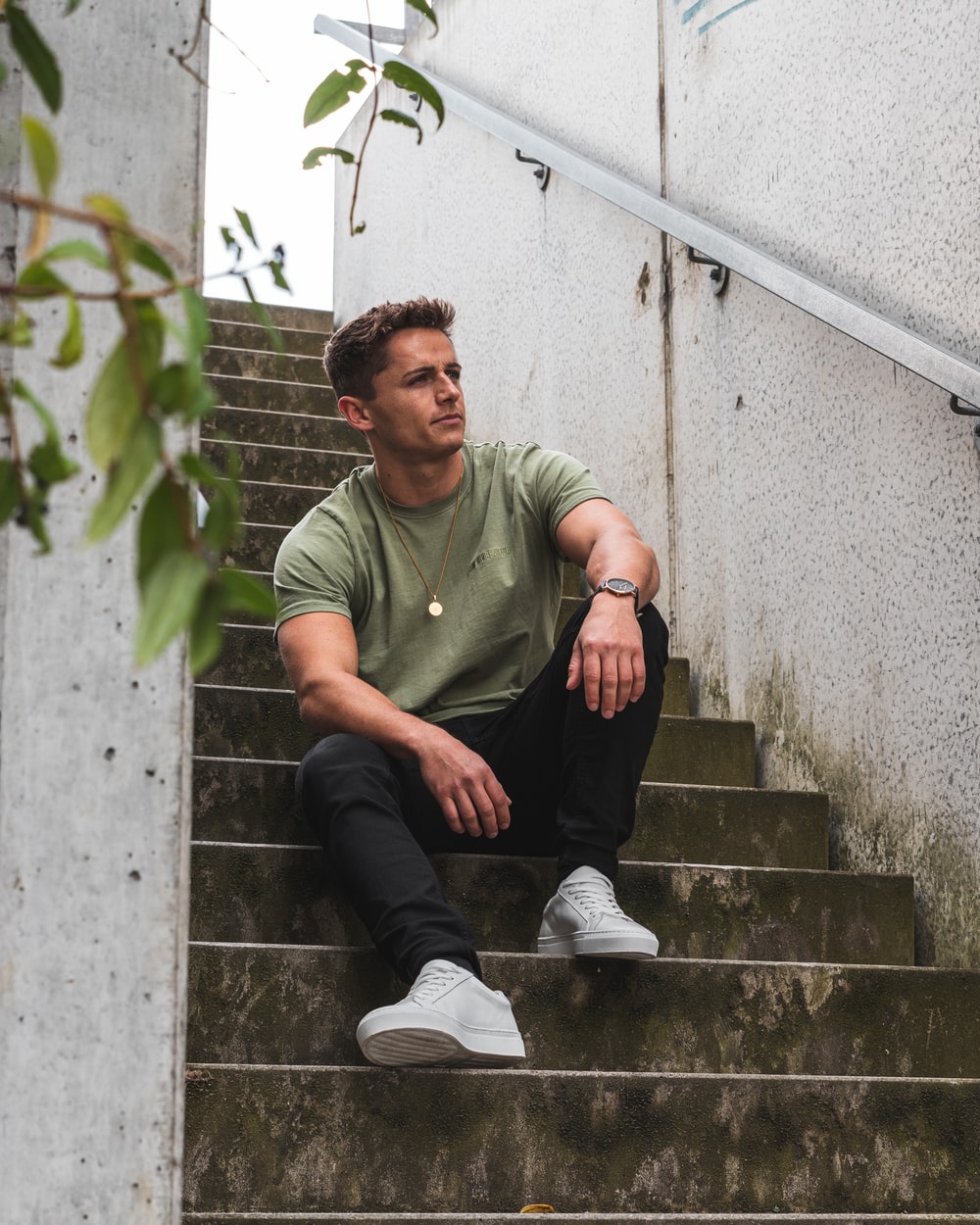 menswear man in green polo shirt and black pants sitting on gray concrete stairs