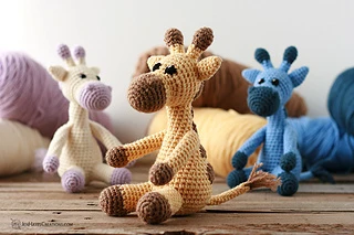 three different colors of crochet giraffes sitting on floor