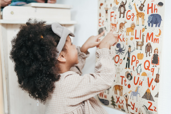 A preschooler pointing to letters on an alphabet poster on a wall.