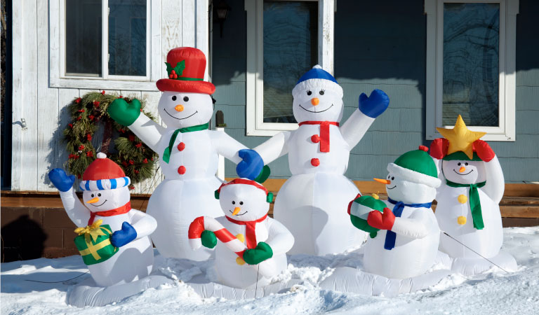 Six inflatable snowman decorations set up in a snowy front yard. 
