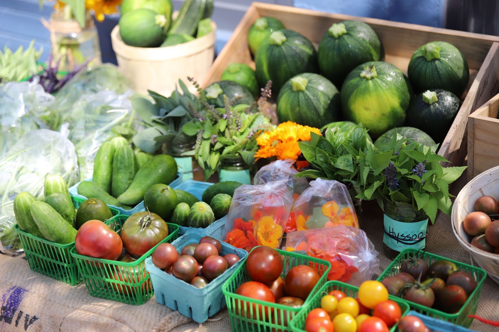 A spread of vegetables including cucumbers, tomatoes, cheery tomatoes and zucchini laid out on a table at a farmer's market.