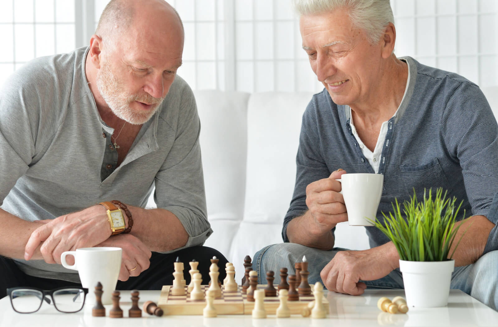 Two seniors playing chess while enjoying a cup of coffee in a brightly lit room.