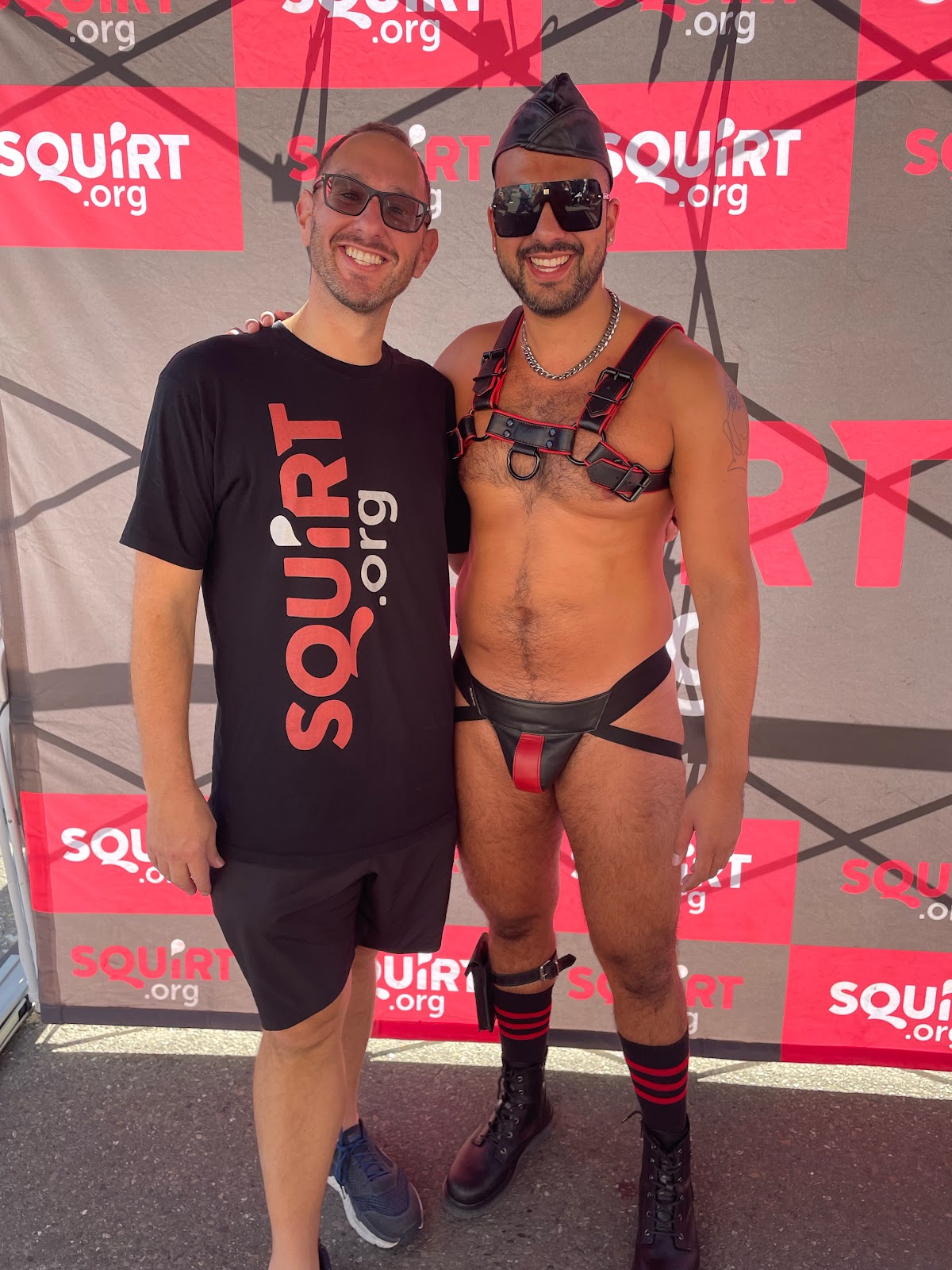 gay onlyfans creator Phil DuChamp wearing a black leather jockstrap and harness posing with a friend wearing a black Squirt.org t-shirt