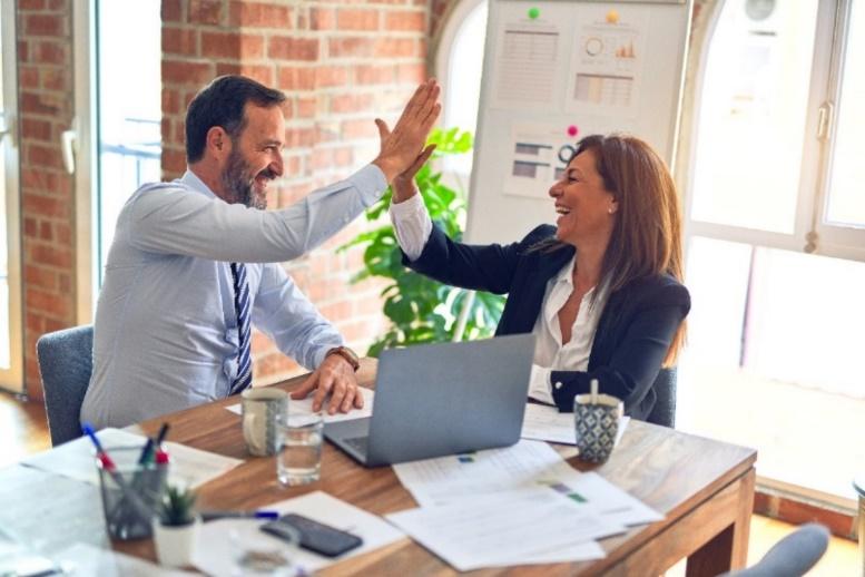 A man and woman wearing professional clothing, smiling and high-fiving each other