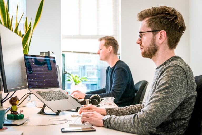 White men sharing a desk, working on computers