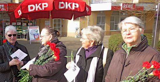 Vier Frauen am DKP Sonnenschirm mit Nelken und Flugblättern.