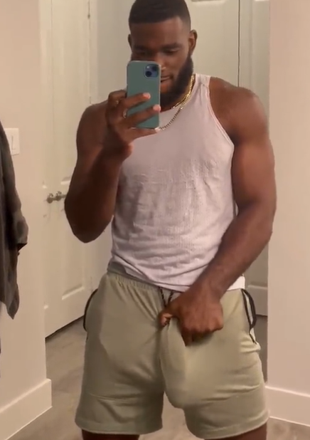 Marshall Price wearing a white tank top while holding his fat hard cock between his green athletic shorts