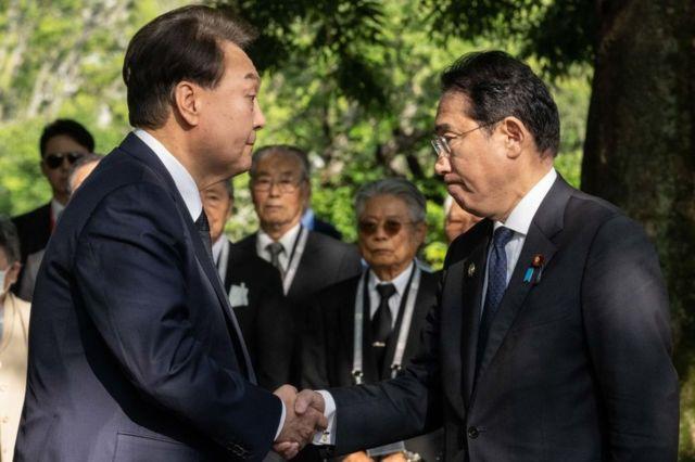 South Korea's Yoon Suk Yeol (L) and Japan's Prime Minister Fumio Kishida shake hands during a visit to the "Monument in Memory of the Korean Victims of the A-bomb" near the Peace Park Memorial during the G7 Summit Leaders' Meeting on 21 May 2023 in Hiroshima, Japan