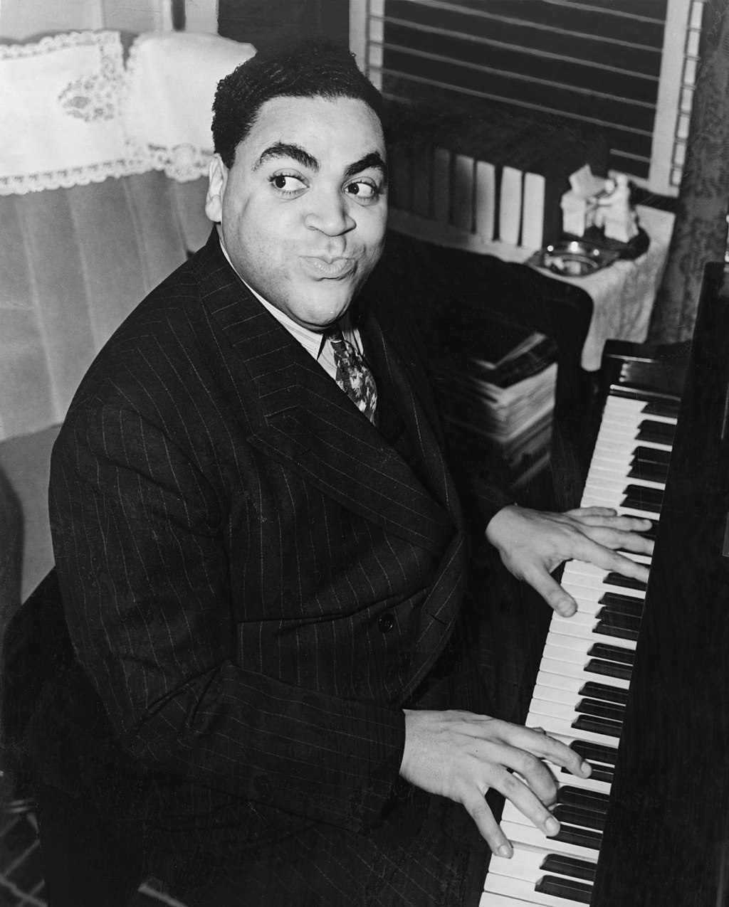 Fats Waller poses while sitting and playing a piano 