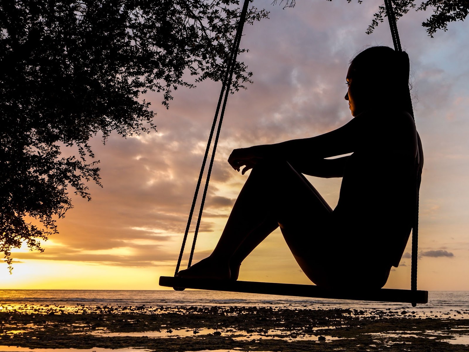 A silhouette of a girl sitting on a swing. 