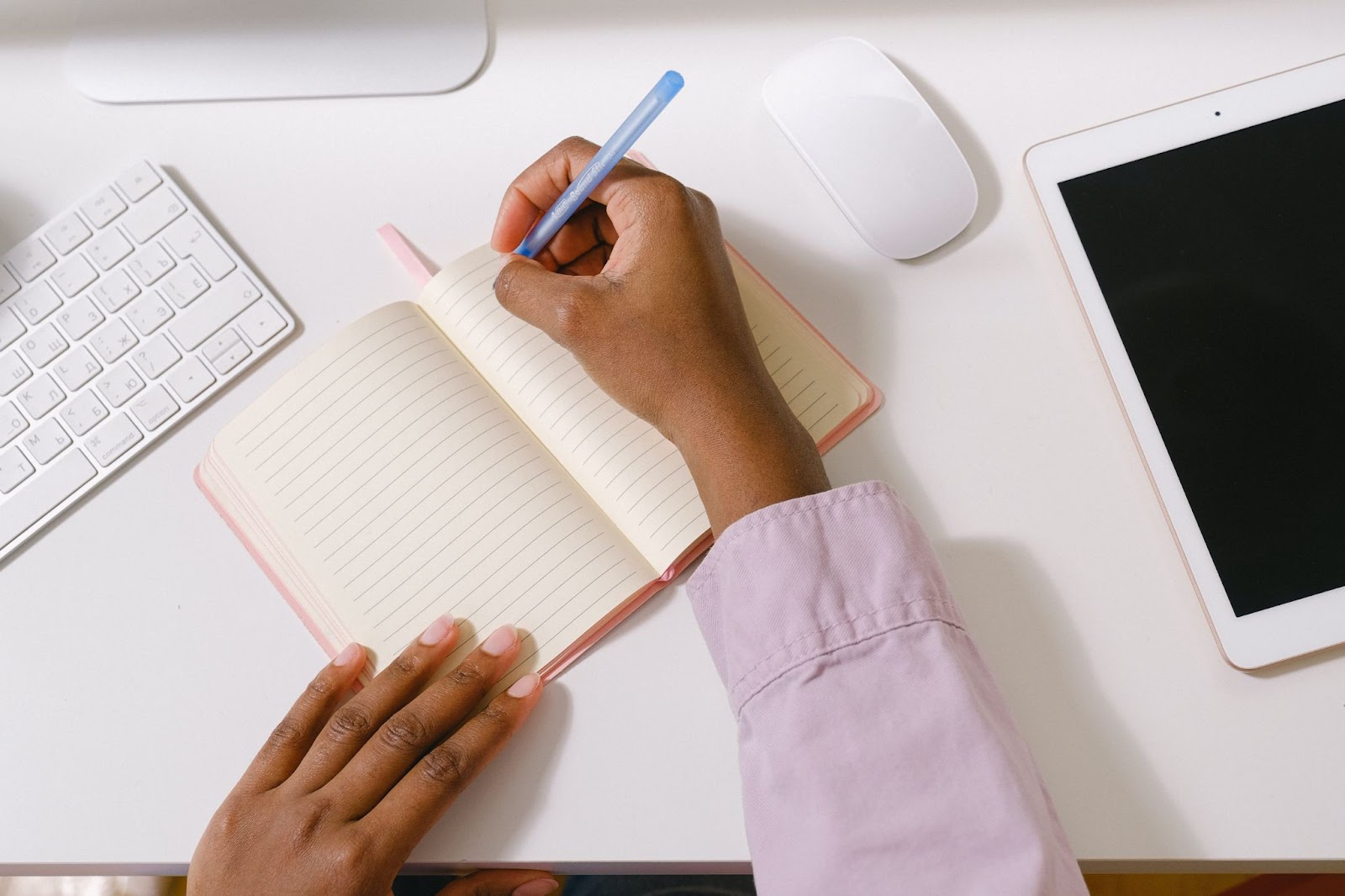 A woman's hand holding a pen and starting to write on a  notebook.