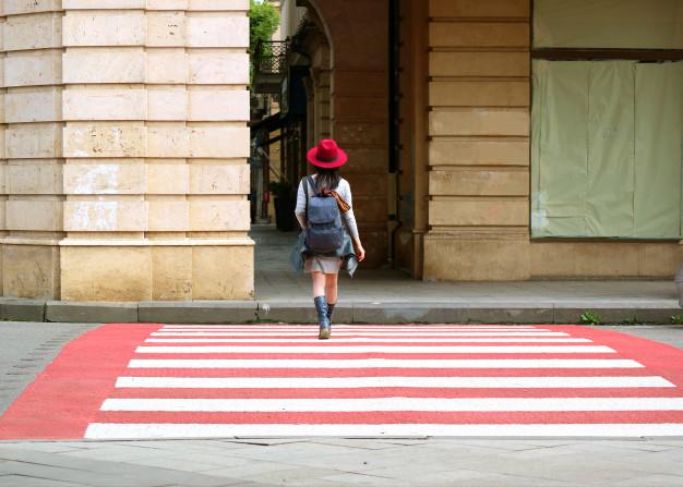 Mujer joven con sombrero rojo caminando sobre el cruce de peatones rojo y blanco Foto Premium