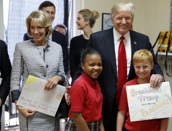 President Donald Trump and Education Secretary Betsy DeVos pose with fourth graders Janayah Chatelier, 10, left, Landon Fritz, 10, after they received cards from the children, during a tour of St. Andrew Catholic School March 3 in Orlando, Florida. 