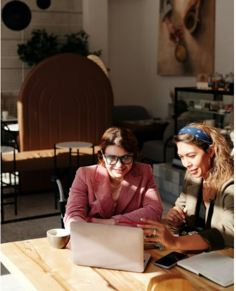 A couple of women sitting at a table looking at a book

Description automatically generated with medium confidence