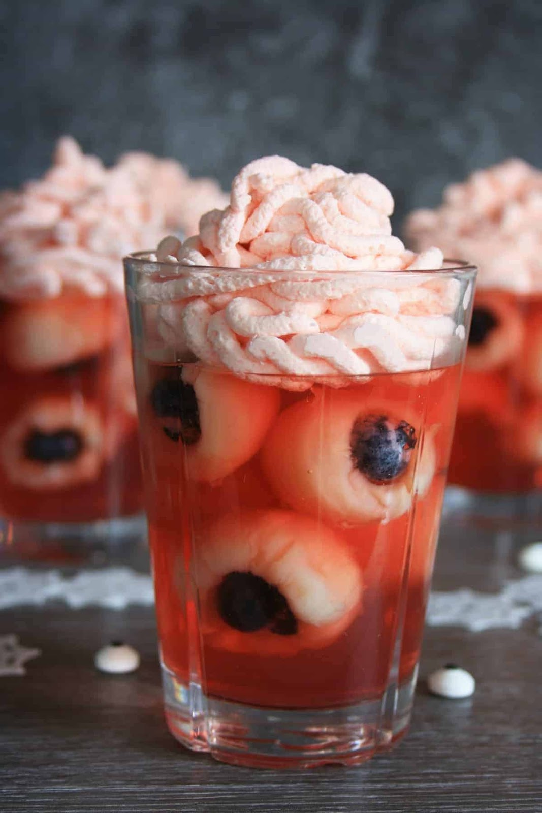 Jelly eyeballs as healthy Halloween desserts, displayed in a glass with whipped cream on top.