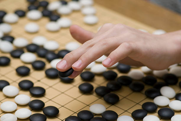 A hand placing a black stone on a go board - How to Play Go Game or Weiqi for Beginners - The Gamerian Gaming Blog