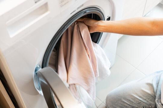 WeServe, a person putting in a pink and white shirts into the white washing machine