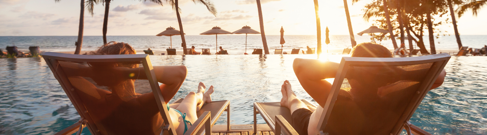 View from behind of two people sitting in pool chairs overlooking an infinity pool and the ocean